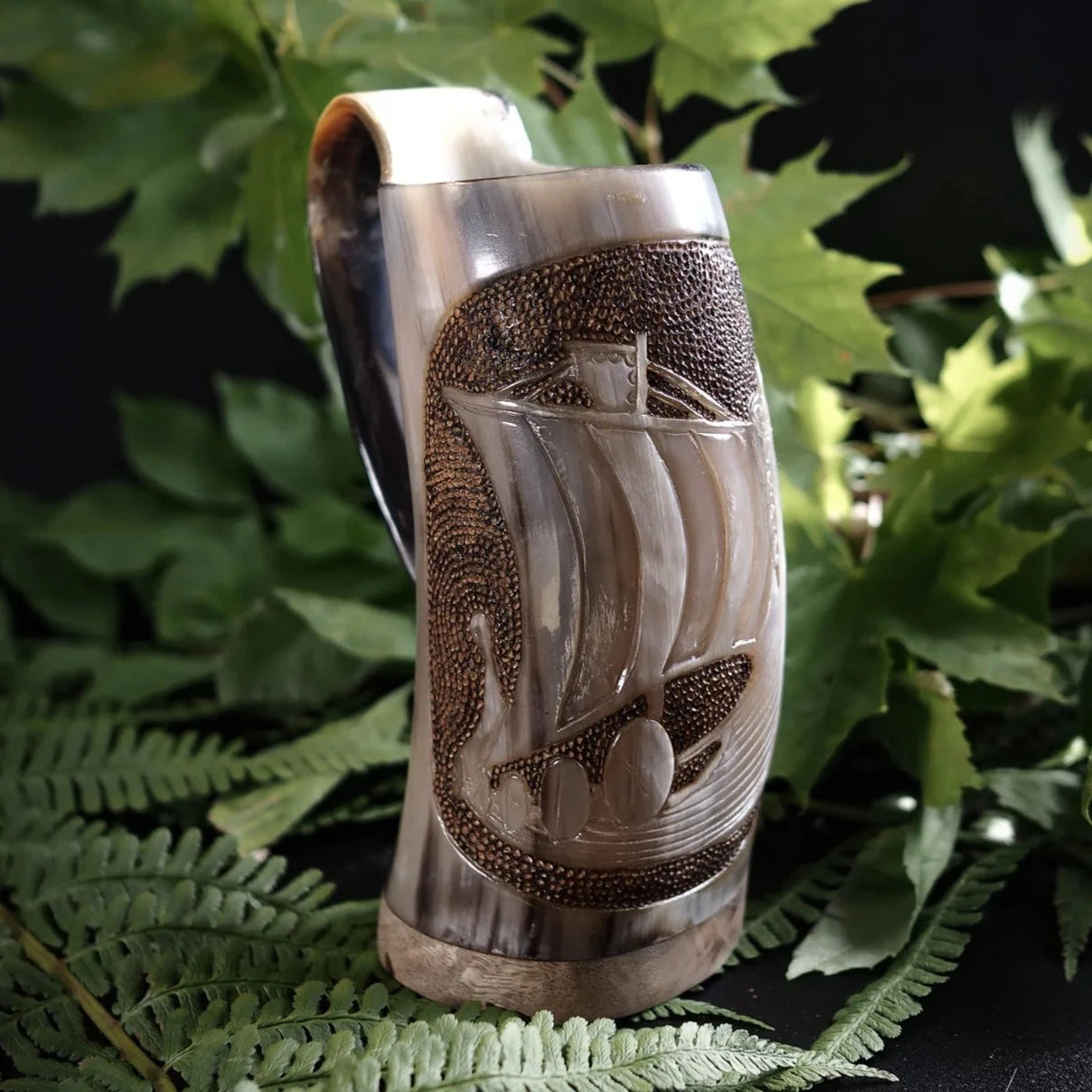 Handsnidad hornmugg i organiskt horn med vikingskepp-motiv. Naturlig hornfärg med mässingsband runt kanten. Traditionell nordisk skärning.