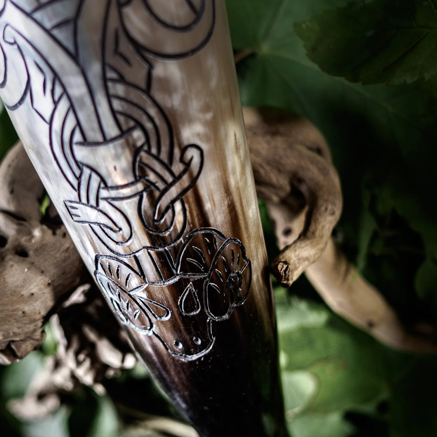 Närbild av graverad hornyta med röd/rosa infärgning som betonar det komplexa norska knotwork-mönstret. Djupa karvningar visar geometriska mönster och interlacing-design i mörkbrunt horn.