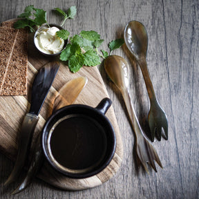 Två ljusa oxhorn-sporks presenterade vertikalt sida vid sida. Båda visar gaffol och skalkis-ändamål. Naturligt horn med kornmönster. Rent, katalog-lämpat produktfoto.