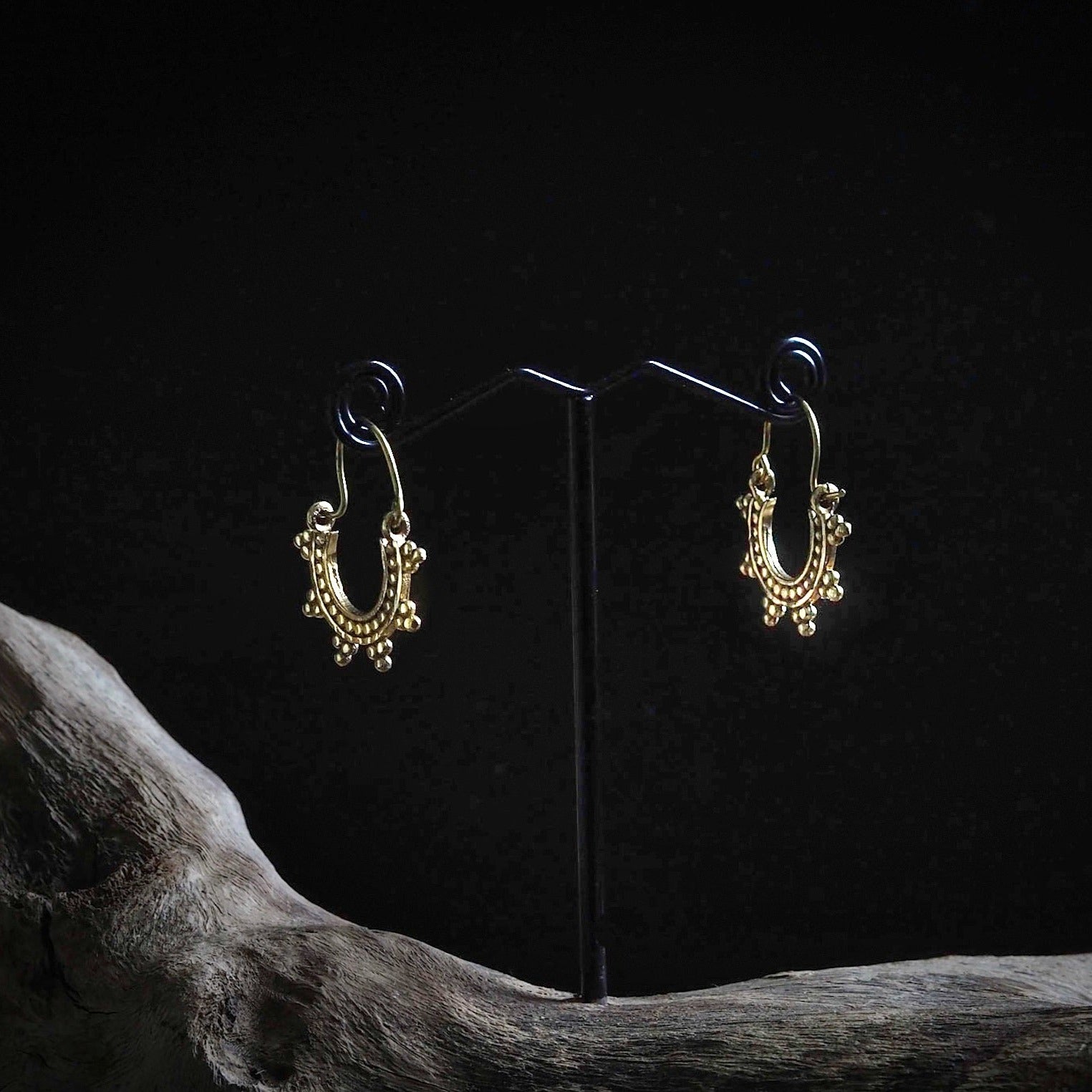 Par guldpläterade örhängen med månformade hängen och detaljerad korndekorering, utställda på svart örhängsställ