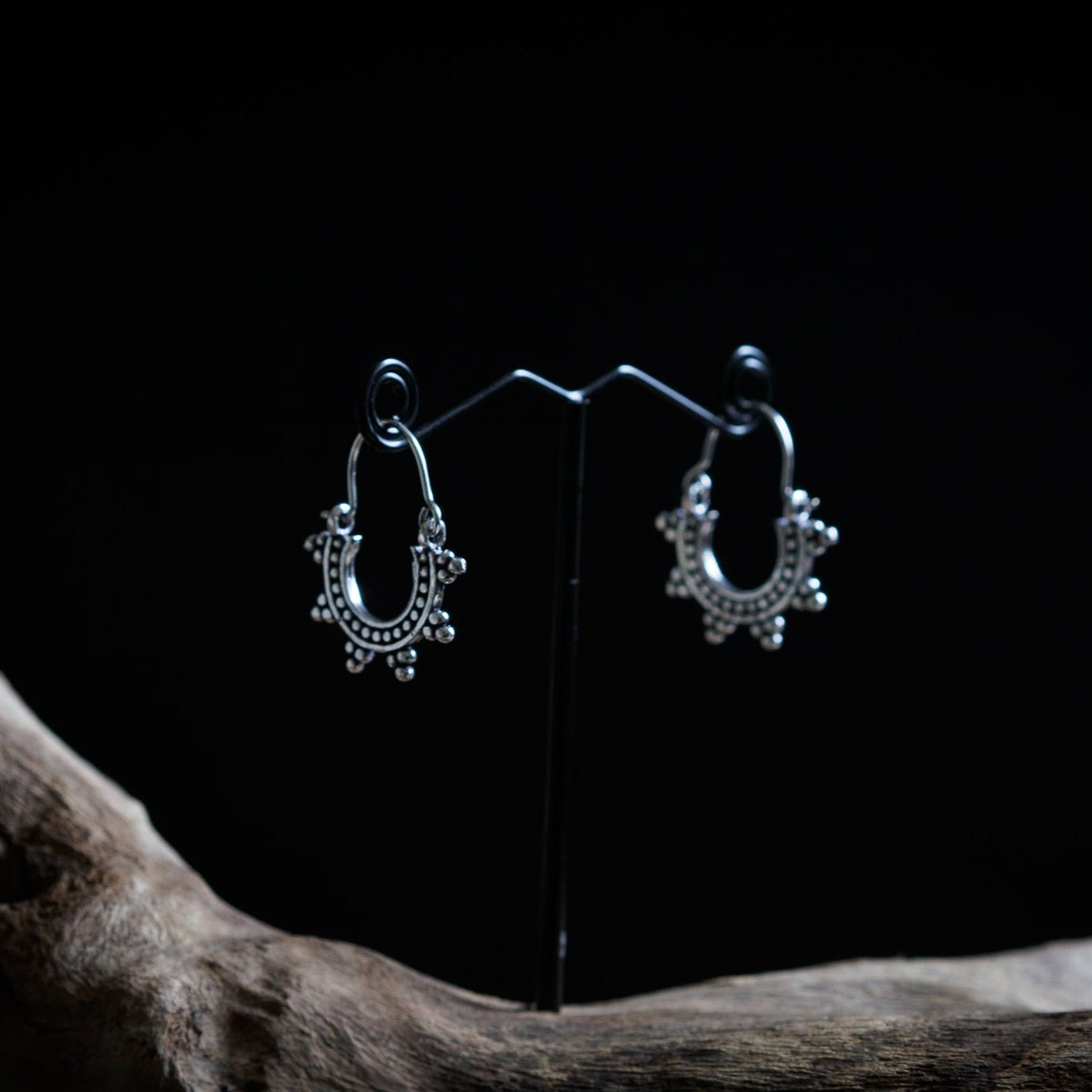 Par små solinspirrerade örhängen i silveröverlagring mässing på presentationsställ, visar ornamentalt design med pärlor och hängande kulor