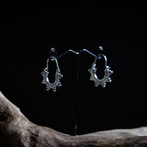 Par små solinspirrerade örhängen i silveröverlagring mässing på presentationsställ, visar ornamentalt design med pärlor och hängande kulor