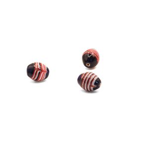 Tre mörkblå glasspärlor med vita och röda ränder, fotograferade från olika vinklar mot vit bakgrund