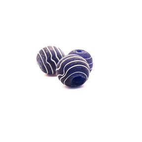 Två blå glaspärlor med vit dekor och frostad yta mot neutral bakgrund