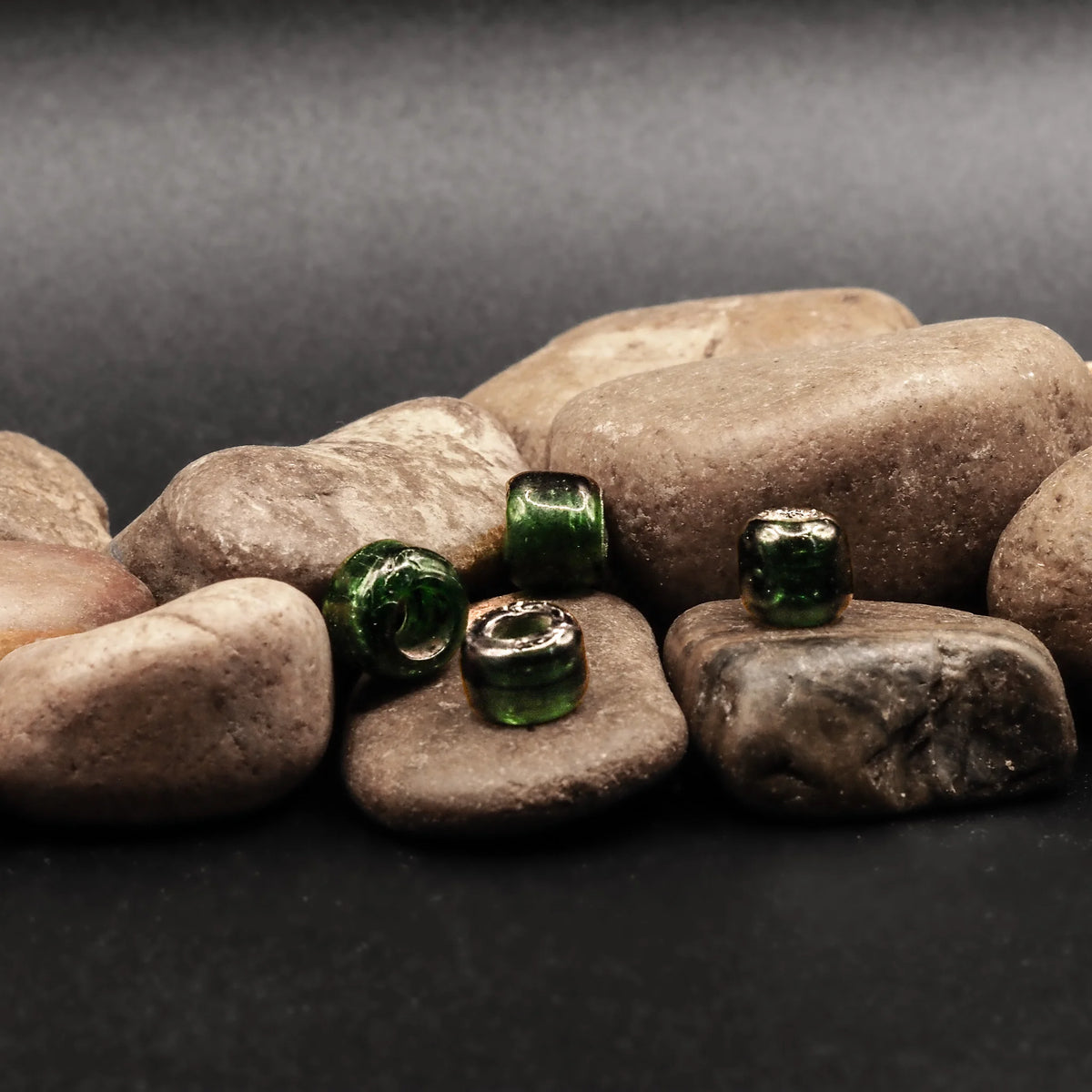 Flaskgrön glaspärla med stort hål fotograferad mot stenig bakgrund. Autentisk vikingaperla för smycken och craftwork.