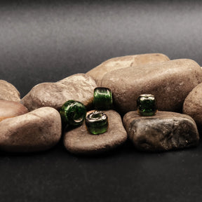 Flaskgrön glaspärla med stort hål fotograferad mot stenig bakgrund. Autentisk vikingaperla för smycken och craftwork.