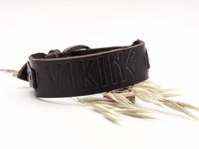 Brunt läderarmband med graverade vikingruna 'VIKING' på vit bakgrund, presenterad med torrt hö och metallspänne