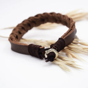 Mörkbrunt läderarmband med handgjord väx-detalj och silvrig metallstängning, displayerat på torkade växtfibrer