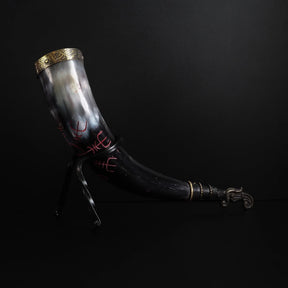 Dryckeshorn liggande. Organisk hornmaterial graverad med korp och vikingaskepp. Runor arrangerade runt ett cirkelformat motiv. Klassisk vikingahantverksutföring.