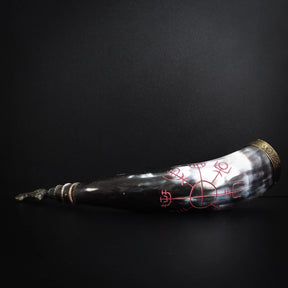 Graverad dryckeshorn med mörkt horn och roströda graveringar. Runsymboler och vikingamotiv utformade i cirkelformat mönster. Mässingsbåge synlig vid öppningen.