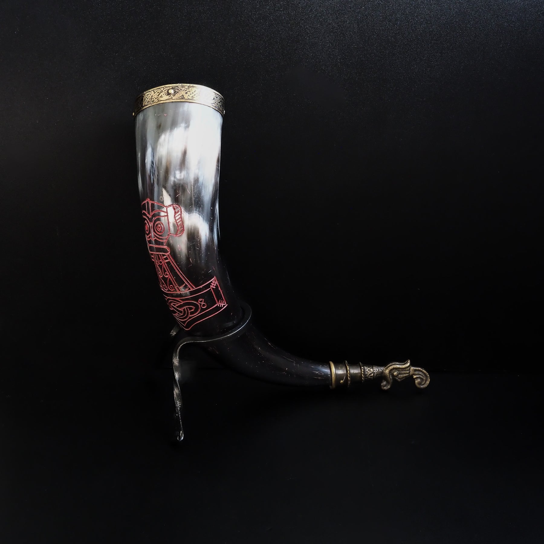 Dryckeshorn framifrån visar vikingmotiv i rött på creamfärgat horn. Korp-gravyr med geometriska monster under.