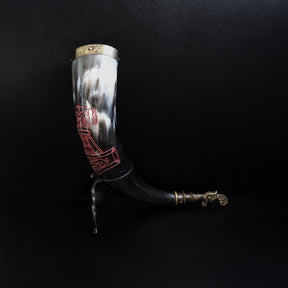Dryckeshorn framifrån visar vikingmotiv i rött på creamfärgat horn. Korp-gravyr med geometriska monster under.