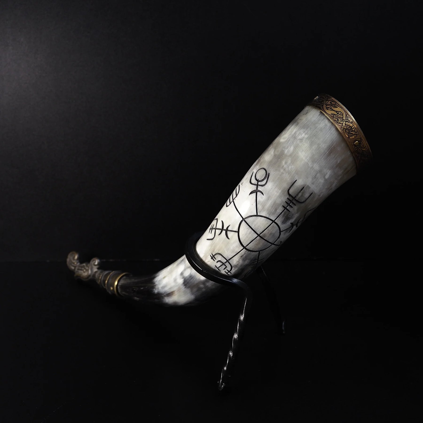 Dryckeshorn i högt läge, visar kontrasten mellan ljust horn vid bägaren och mörkt spetsigt horn. Graverade runor och vikingamotiv. Mässingsbåge och dekorativ slut.