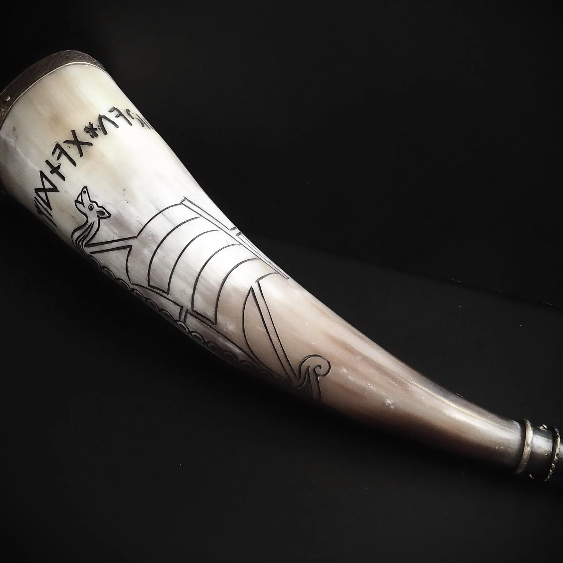 Dryckeshorn från sidan med utbredda korpvingar i gravyr. Ljust horn med dunkelgrå mönster och mässingsdetaljer synliga.
