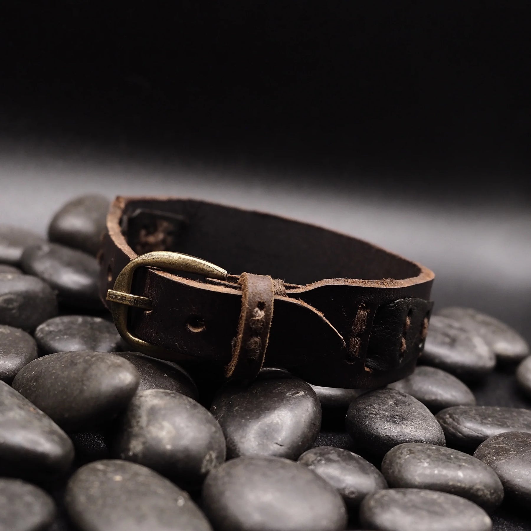 Sidovy av brunt läderarmband på stenar, visar naturlig patina och tröghet från användning, metallspänne synligt