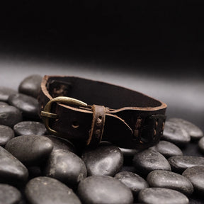 Sidovy av brunt läderarmband på stenar, visar naturlig patina och tröghet från användning, metallspänne synligt