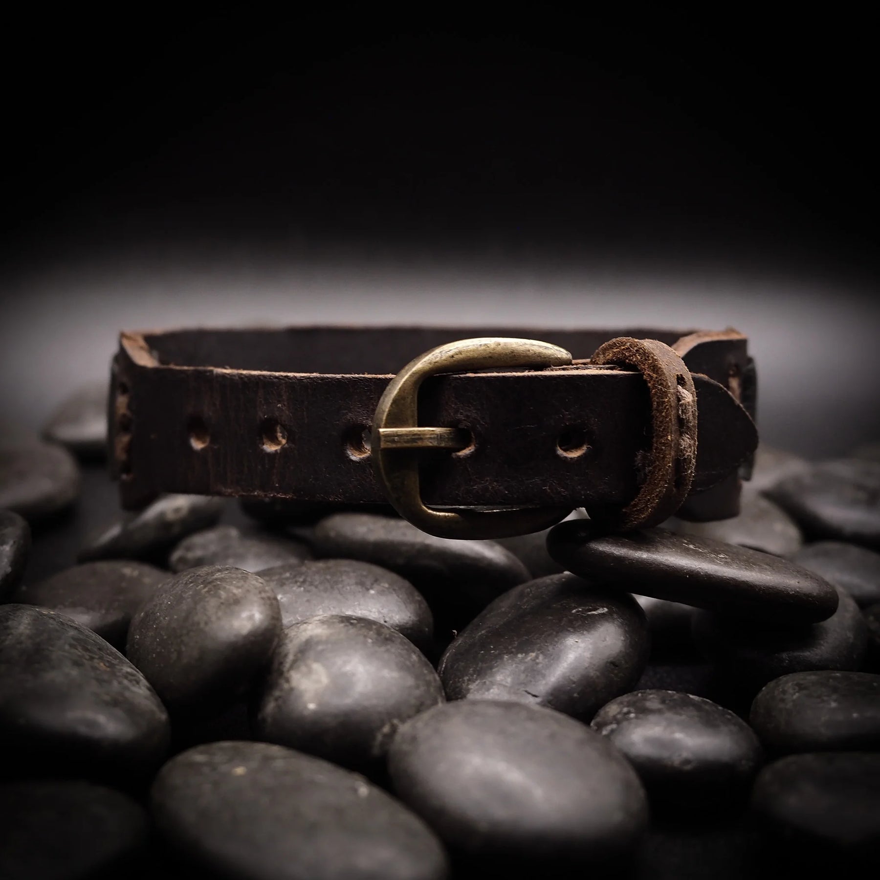 Brunt läderarmband med metallspänne på vita bakgrund med dekorativa stenar, visar produktens ålder och kvalitet