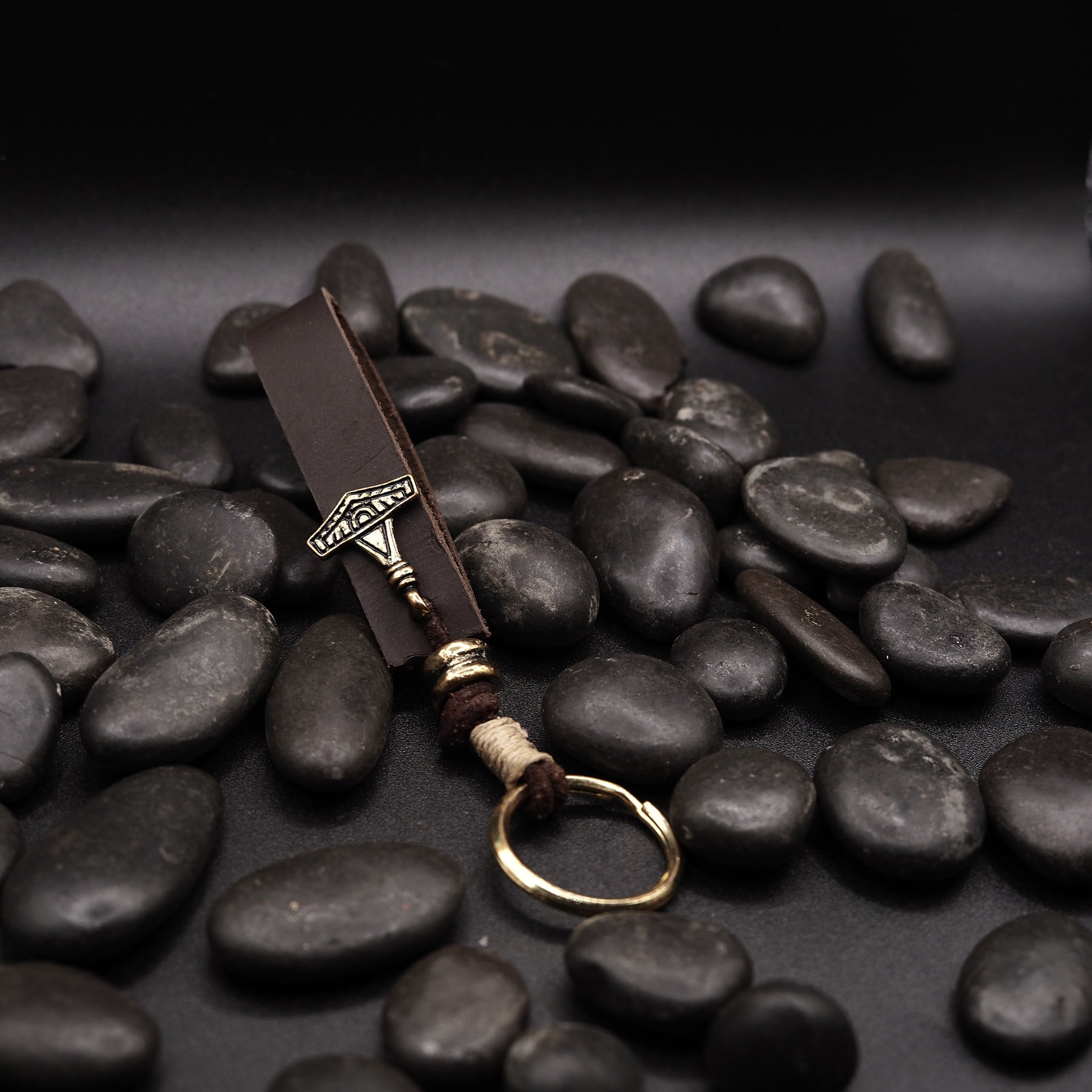 Nyckelring av lädre med liten Torshammare-amulett i brons, lagd på svarta stenar.