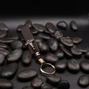 Nyckelring av lädre med liten Torshammare-amulett i brons, lagd på svarta stenar.