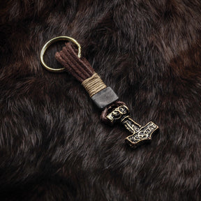 Samma Torshammare-nyckelring på mörkare botten, visar patinerad brons och läderbandet.