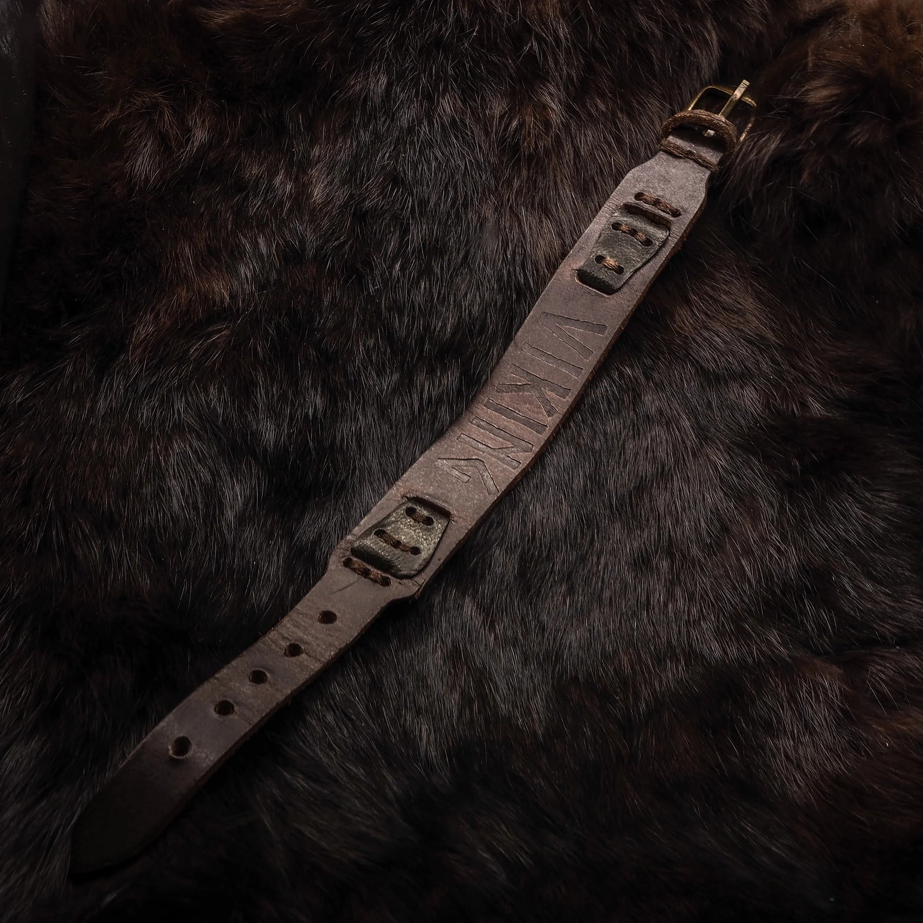 Överblick av brunt läderarmband med metallnitar på mörk bakgrund, visar full längd och detaljerad konstruktion