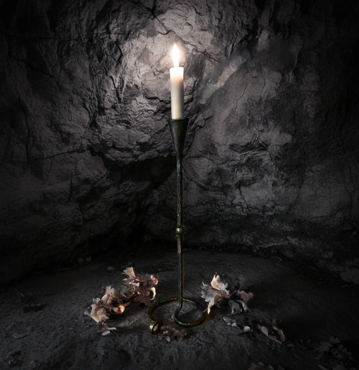 Lavatein ljusstake i hand-smiddat järn med tändstjärne som glödar inuti en mörk stenkavern. Dramatisk belysning framhäver den vikingska estetiken och det råa järnens finish.