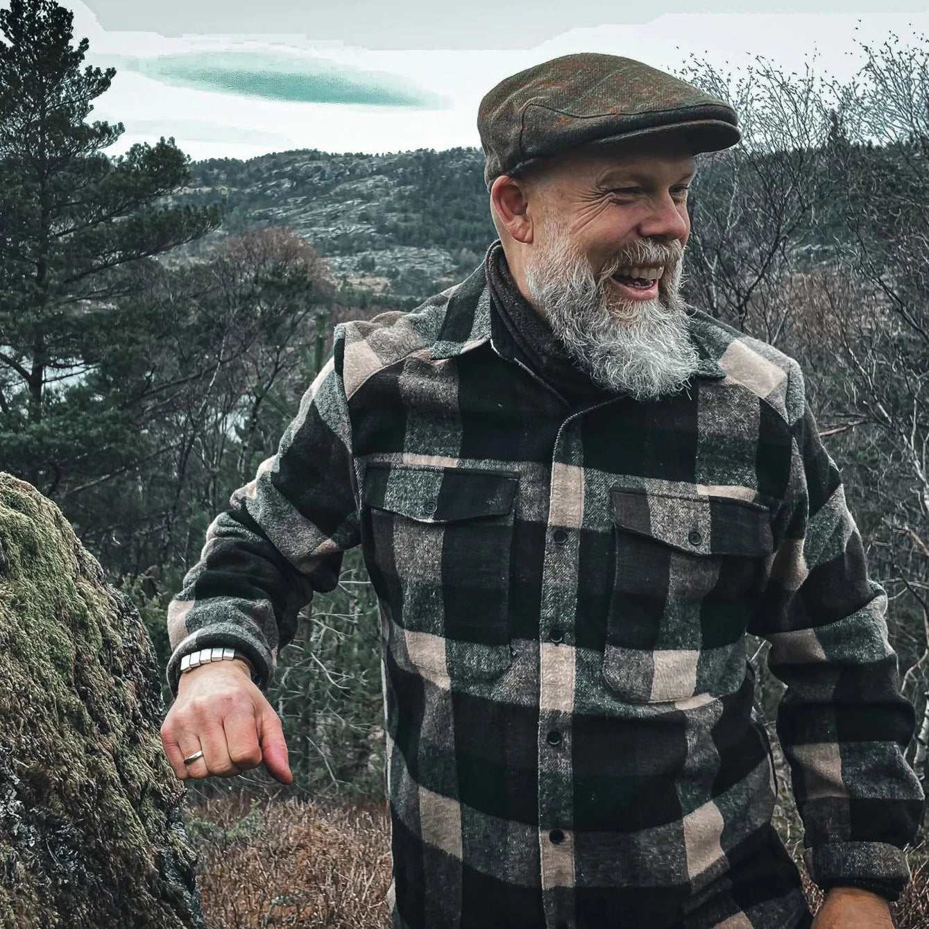 Bearded man in plaid shirt photographed outdoors in mountainous landscape setting, lifestyle branding image
