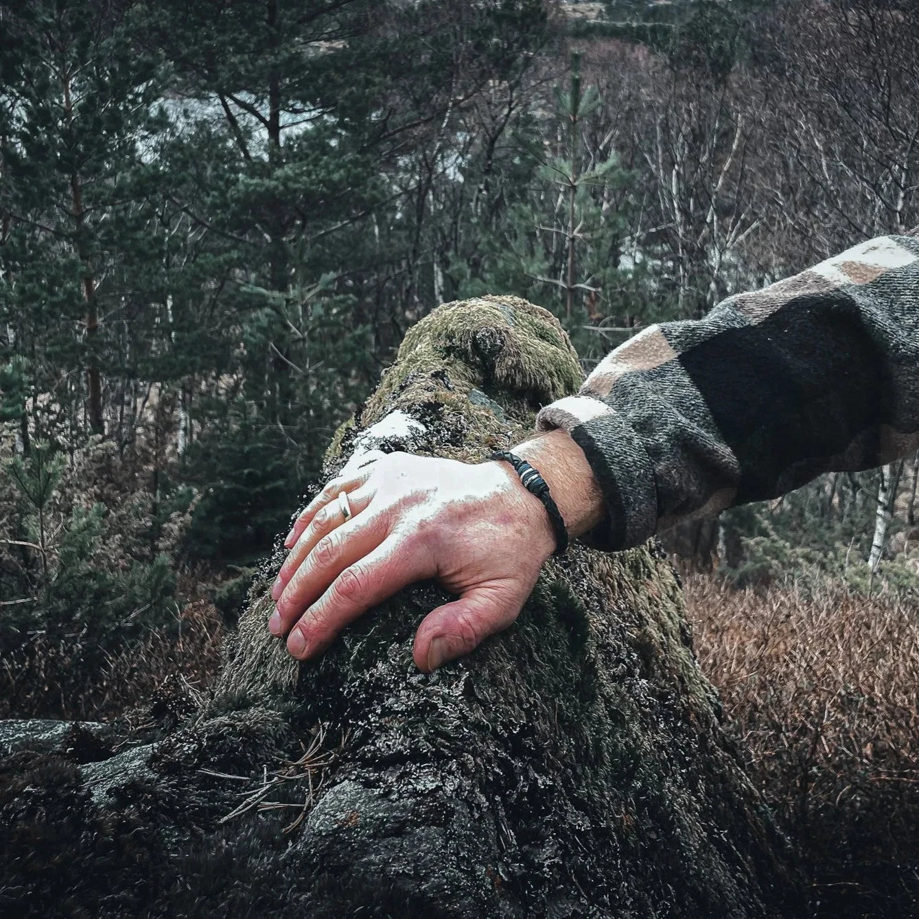 Svart läderarmbandet Eitre Vikinga med metallband på arm mot mossig sten i skogsomgivning