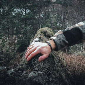 Svart läderarmbandet Eitre Vikinga med metallband på arm mot mossig sten i skogsomgivning