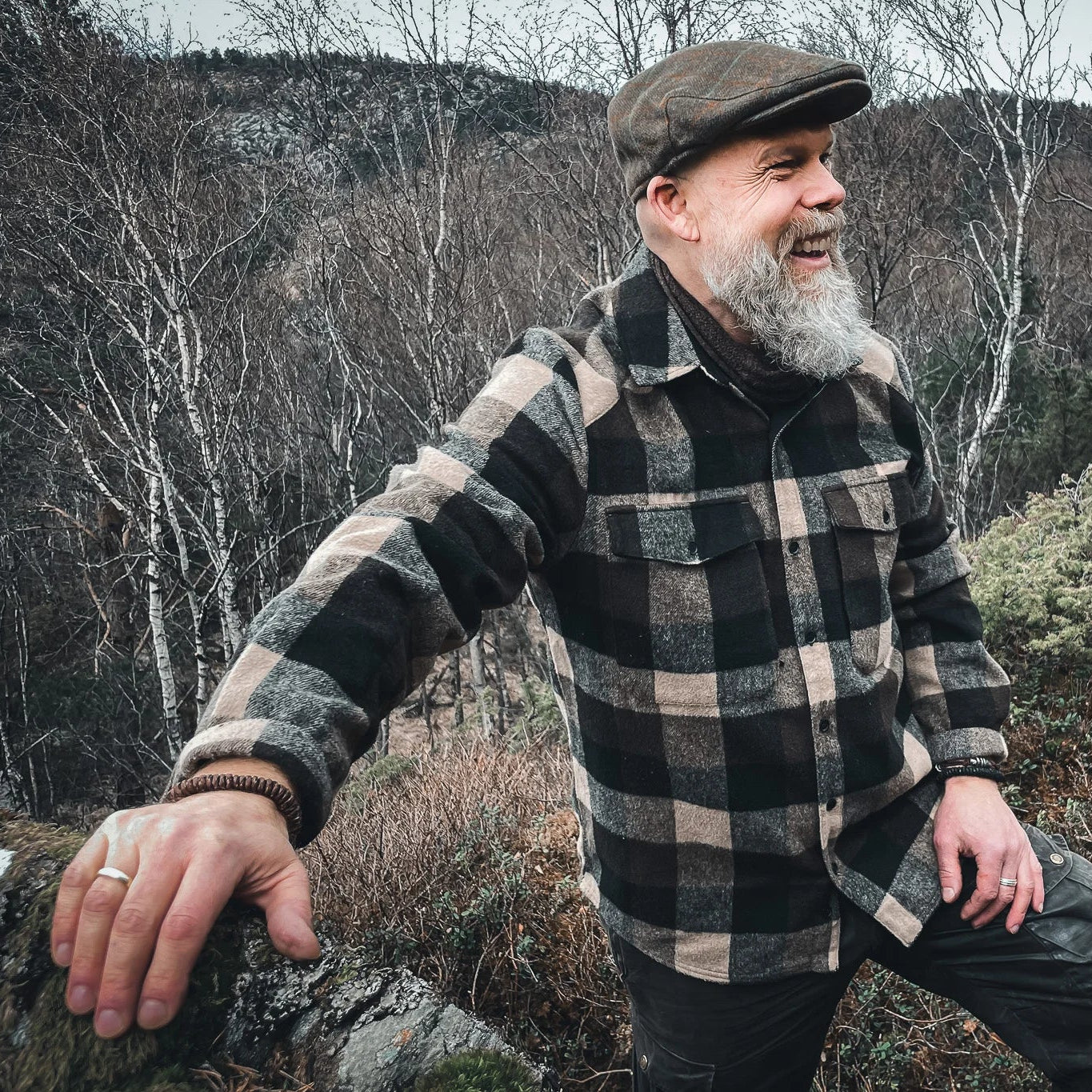 Lifestyle-foto av brunt brokk-armband på en mans handled. Han bär en ruttig jacka och keps, fotograferat mot naturlig utomhussceneri.