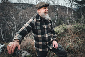 Lifestyle-foto av brunt brokk-armband på en mans handled. Han bär en ruttig jacka och keps, fotograferat mot naturlig utomhussceneri.