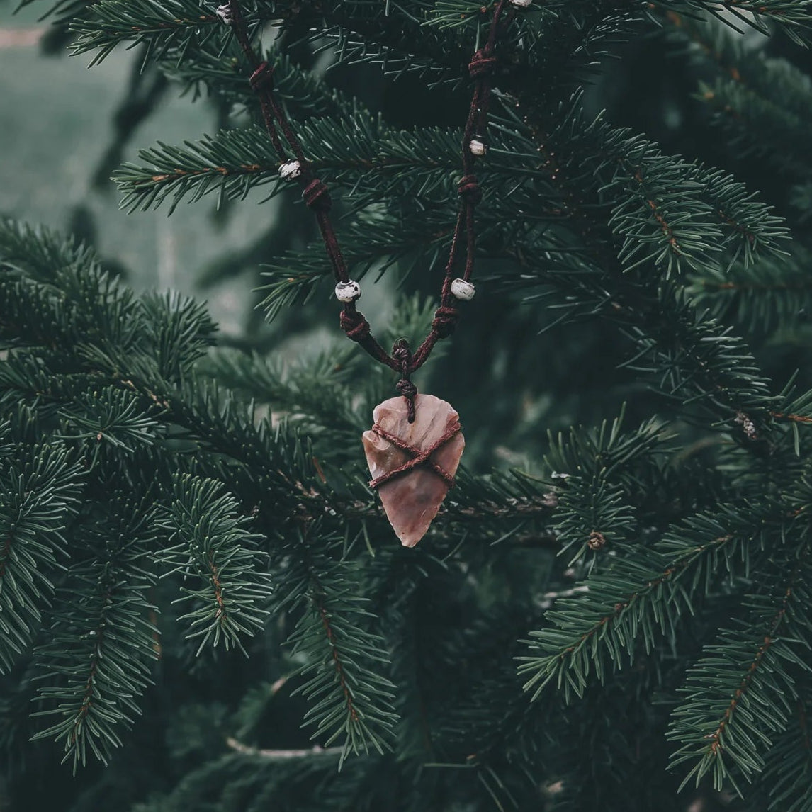 Halsband pilspets med handgjord stenpilspets från neolitisk tid, läderband och benpärlor, visat på granar