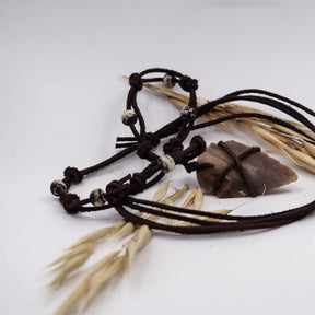 Pilspetshalsbandet på vit bakgrund med ljusbeige stenspets lindad i mörkbrunt snöre. Två läderband med benärlor vid knop. Vete och naturliga fibrer runt anhänget. Detaljerad produktfotografi som visar autentisk neolitisk karaktär och mineralfärg.