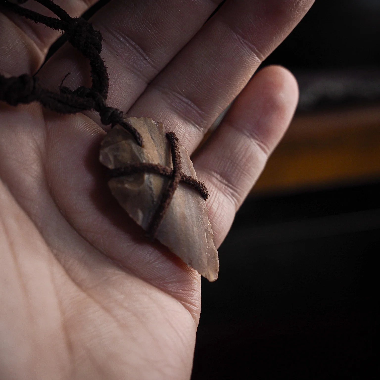 Pilspetshalsbandet på vit bakgrund med naturlig styling. Ljustan stenspets med naturliga strieringar lindad i mörkbrunt snöre. Läderband med benärlor omgivna av vete och torkade gräs som framhäver handgjort, vikingakänsla.