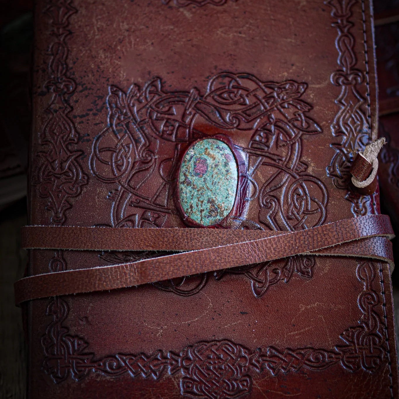 Handgjord läderbok Kristall i medium med rubin och fuxit-sten. Burgundibrunt präglat läder med vikingdekor, rödviolett sten med iriserande glans i metallfattning och bruna läderband.