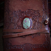 Handgjord läderbok Kristall i medium med rubin och fuxit-sten. Burgundibrunt präglat läder med vikingdekor, rödviolett sten med iriserande glans i metallfattning och bruna läderband.