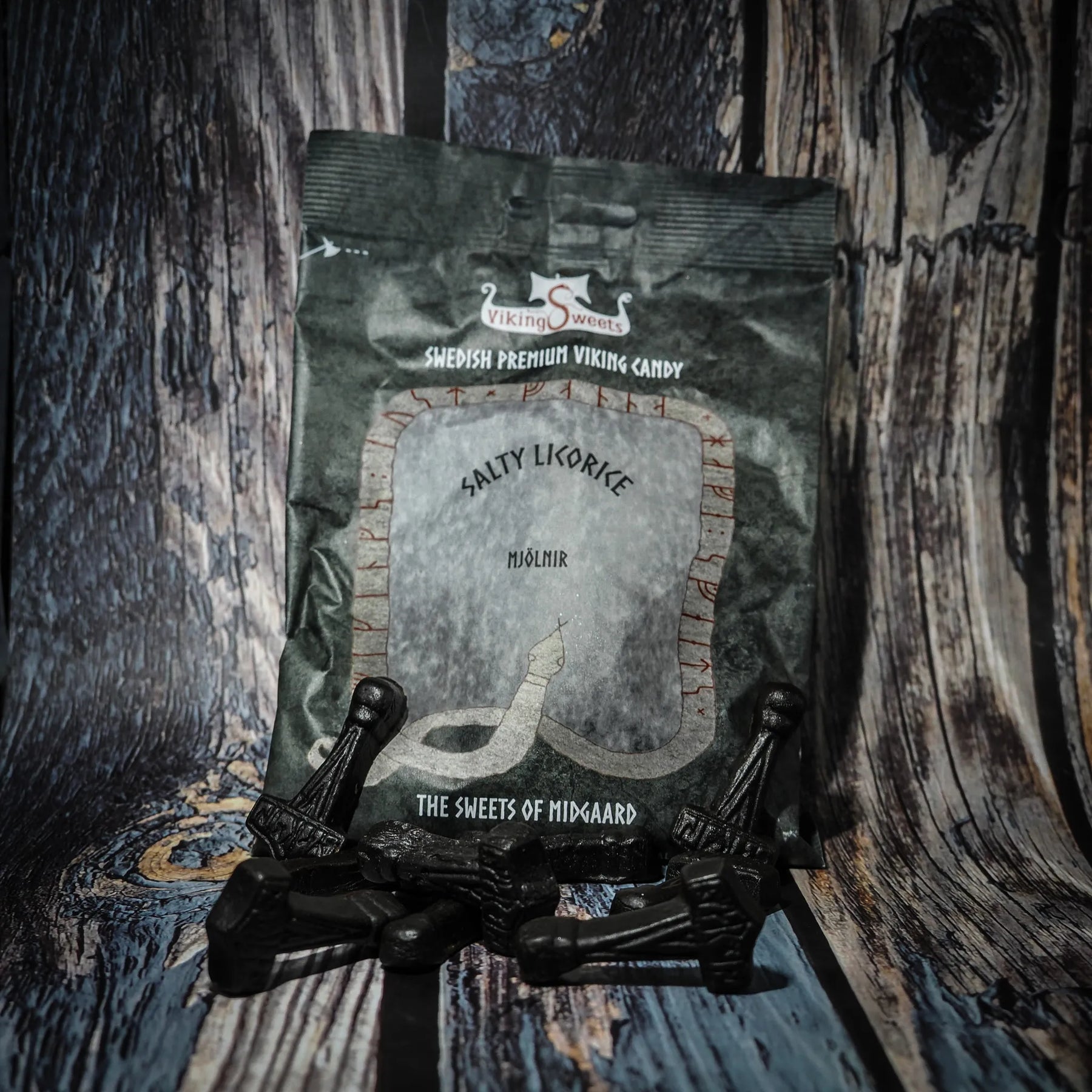 Fyra paket vikinggodis med Mjölnir-formade sura karameller arrangerade på trä. Paketen är röda, svarta och beiga med silvrig text.