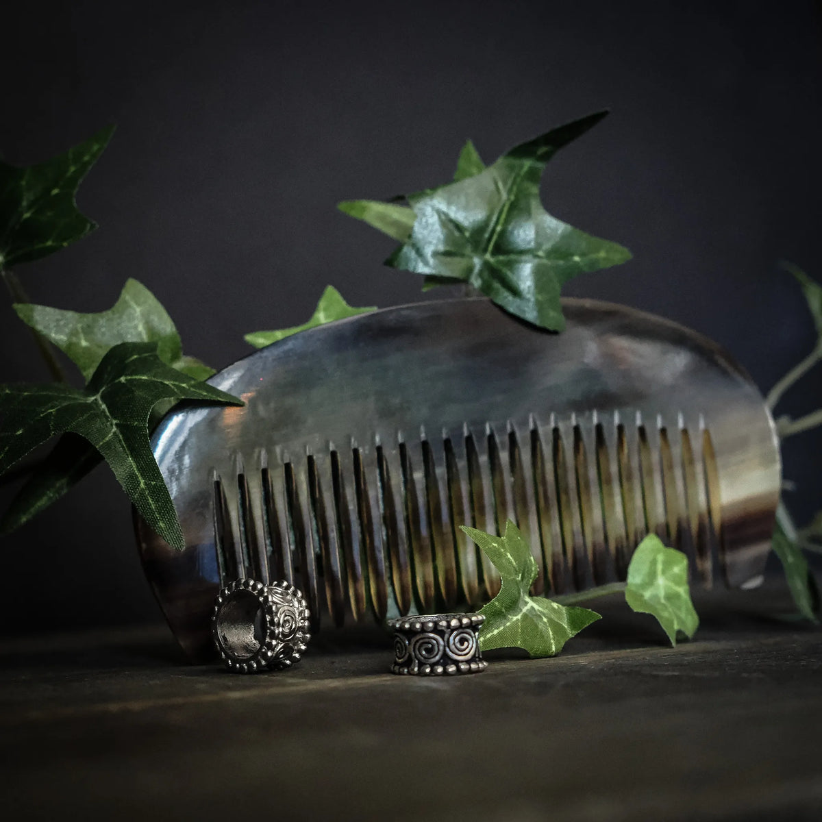 Hår-set till henne: Horn kamma (10x4 cm) med fina tänder och två silver-platerade mässings-pärlor på träyta omgiven av gröna blad.