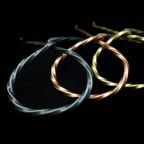 Tre hornställ i smide visade sida vid sida: järnsvart variant till vänster, mässing i guldton i mitten, och ljusare mässing till höger. Alla med vridna metalldetaljer.