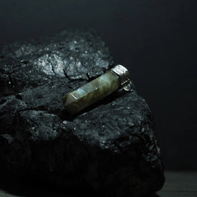 Labradorit-kristallhänge på mörkblå snöre, hängande mot mörk bakgrund. Stenens iriserade ljusblixtar dramatiskt belyst. Metallfattning med smyckesdetaljer. Lifestyle-produktfoto för halsbandspresentering.