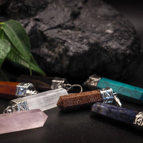 Stenhängesamling med flera olika stenar: röd guldsten, klart kvarts, mörkblå och turkos stenar, alla monterade i silverfärgad mässing på mörk botten