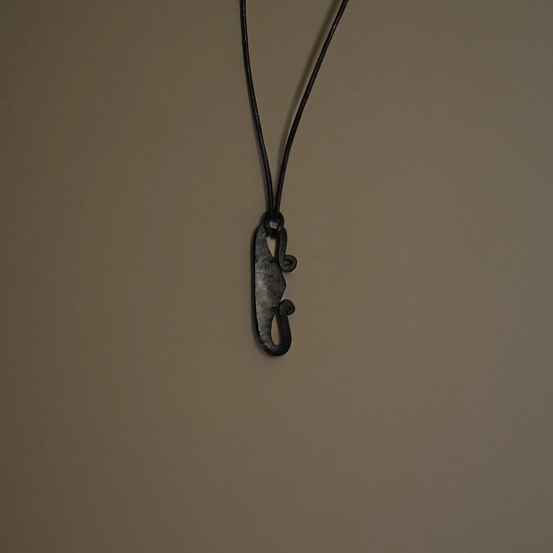 Eldstålspendant av järn hängande på svarta snören mot neutral bakgrund, visar Nordic verktygsformning