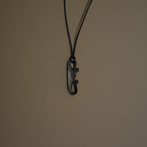 Eldstålspendant av järn hängande på svarta snören mot neutral bakgrund, visar Nordic verktygsformning