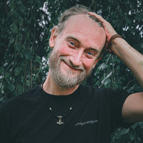 Porträtt av en äldre man med grått skägg fotograferad utomhus, bärande svart nordlysviking.com t-shirt med antydd Thors hammare-pendant