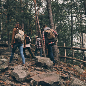 Tre personer med ryggsäckar vandrar uppför klippig skogsled, livsstilsbild för visselpipa