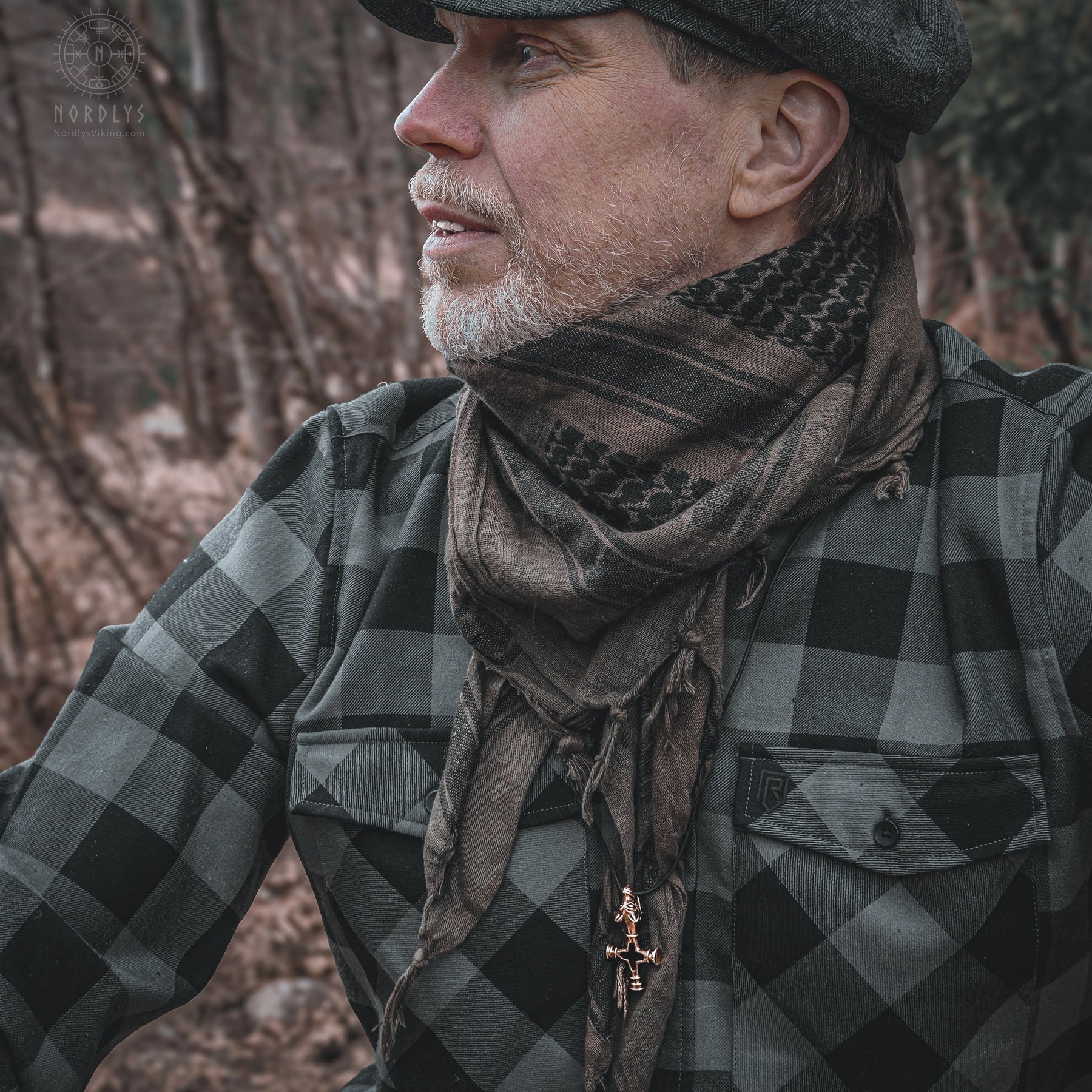 Man in Nordic traditional dress wearing bronze Vargkors (wolf cross) pendant on dark cord, side profile in forest setting