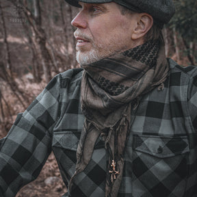 Man in Nordic traditional dress wearing bronze Vargkors (wolf cross) pendant on dark cord, side profile in forest setting
