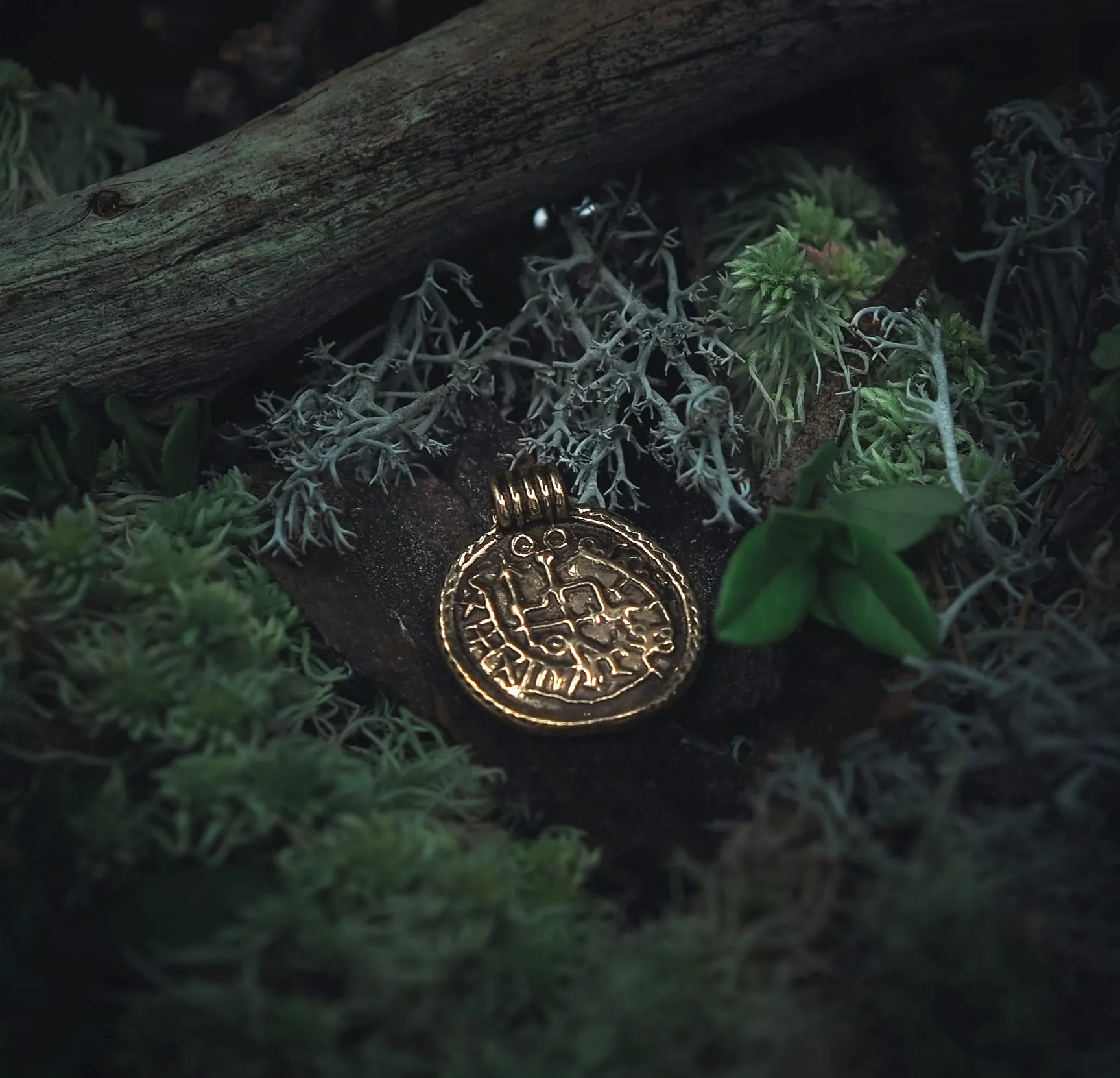 Skyddsamulett i brons med vikingrunor och brakteatdesign på snörknagg, fotograferad i naturlig skogsmiljö
