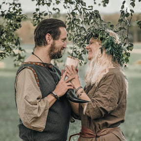 Vikingbröllopsceremoni - par i autentisk vikingkostym utbyter dryckeshorn under hängande löv, visar tradering bröllopspacket i praktisk användning