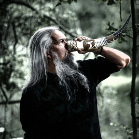 Livsstilsfotografi av dryckeshorn med vikingaskepp pyrografi. Visar händer som håller hornet för drickande, med detaljerat snidmönster av segelfartyg.